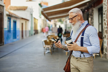 Happy fashionable man drinking coffee and using smart phone on a city street - Fashionable senior boy having fun with web application - Technology trends and cheerful elderly lifestyle concept 