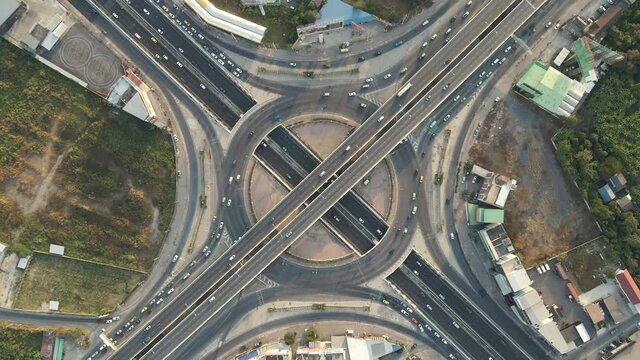 Top-down aerial drone shot of roundabout and x-shaped crossing expressway with evening busy traffic.