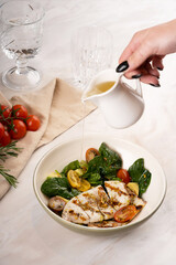 A woman's hand pours oil on a salad with squid and vegetables. Seafood. Restaurant food. Menu. 