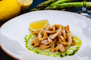 Deep fried squid rings or calamari with sauce and lemon on white plate.