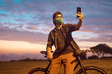 atractivo hombre joven maneja feliz en bicicleta por un parque por la ciudad. Modelo ciclista en mascarilla 