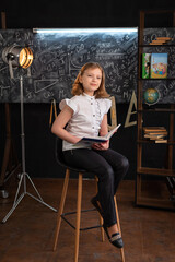 a girl in school clothes sits on a chair with a textbook in her hands