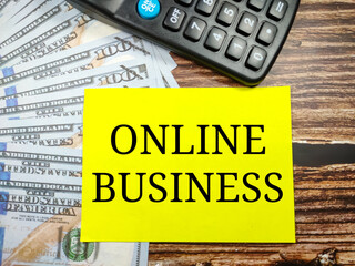 Business concept.Text ONLINE BUSINESS with banknote and blur calculator on a brown wooden background.