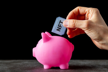 Concept image for investing in Non Fungible Tokens known as NFT s. These are digital data files of value that are traded through Ethereum blockchain. A woman is putting one into a piggy bank.