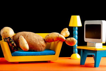 A quirky metaphorical concept image showing a potato man lying on a couch watching tv in a living room setting. Image for being couch potato, obesity, sedentary lifestyle and health effects.