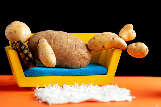 A quirky metaphorical concept image showing a potato man lying on a couch in a living room setting. Image for being couch potato, obesity, sedentary lifestyle and health effects.
