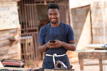 young african carpenter smiling while using his phone