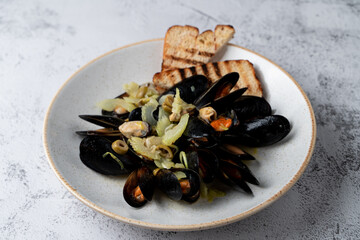 A portion of mussels with celery and chili flakes on a light gray stone background with crunchy croutons