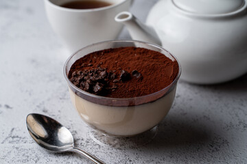 Classic tiramisu in a plastic glass with a spoon and tea set aside