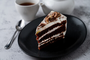 Layered nut pie with walnut and moist sponge on a black plate in a soft light