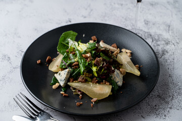 Close up of pear and gorgonzola salad with nuts and mixed salad, black plate, fusion cuisine