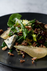 Fototapeta na wymiar Close up of pear and gorgonzola salad with nuts and mixed salad, black plate, fusion cuisine