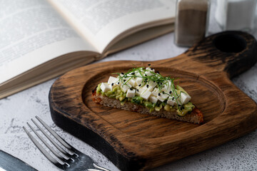 Avocado toast on a wooden board, on a beautiful stone table with open book, slow morning, minimalist morning