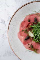 Close up of tuna carpaccio on a stylish white plate with arugula and sun dried tomatoes, half...