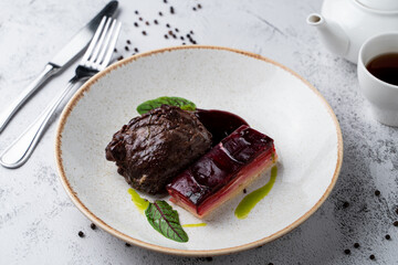 Soft cheeks with special cheese beetroot sauce and mashed potato on white stone table in a wide restaurant bowl, magazine photo