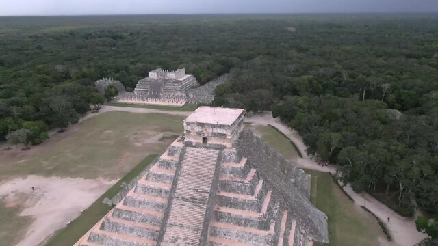 Aerial Tilt Down Shot Of Chichen Itza Amidst Trees Against Cloudy Sky, Drone Flying Forward Towards Famous Historic Landmark