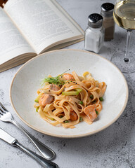 Magazine photo illustration of salmon and avocado  fettuccine on a grey stone table with a glass of wine and open book aside