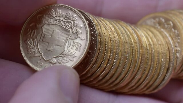 Macro shot of person checking several rare golden vreneli francs in hand. Swiss twenty chf coins.