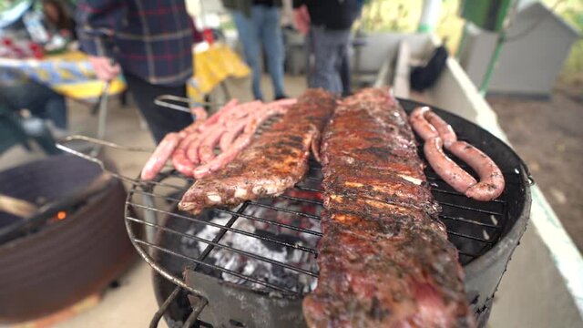 Carne variada sobre barbacoa en el exterior con amigos de fondo