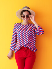 Portrait of young woman wearing sunglasses and hat over a yellow background