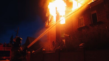 The roof of the house is on fire. The residential building burn, village. Firefighters put out a fire from the crane from above. Smoke and sparks.