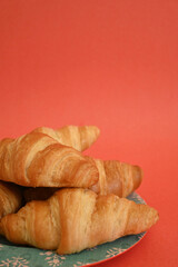 Closeup of delicious homemade golden croissants on turquoise plate on coral background with copy space