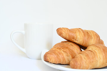 Closeup of homemade golden croissants with white cup of coffee tea with handle and white background with copy space