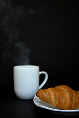 Close-up of delicious homemade golden croissant with cup of hot tea coffee with dark background. Photograph with copy space