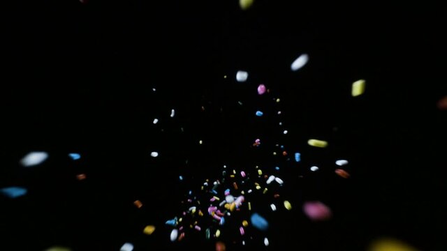 Colorful candy food sprinkles falling and dropping creating hyperspace light speed effect against black background in slow motion