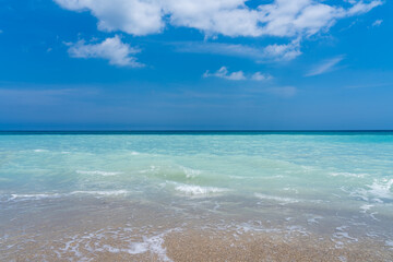 Transparent ocean water splashes on the sandy shore and contrasts with the blue sky
