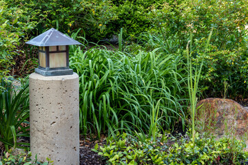 Fototapeta na wymiar Japanese style metal lantern on stone post in tranquil lush green garden