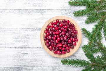 Raw fresh cranberries in wooden bowl and fir branches on light wood background. Top view. Copy space