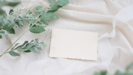 Photostock wedding styled composition. Feminine desktop mockup scene with leaves, silk ribbon, blank greeting card on white textured fabric background. Flat lay, top view.