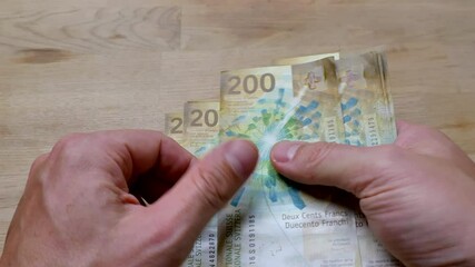 Close up shot of male hand counting several two hundred Chf francs banknotes on wooden table. - Powered by Adobe