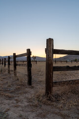 Sunset and an old wooden fence at California desert ranch in Pioneertown with a Joshua tree and mountains in the background.