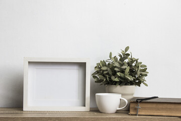Mock up photo frame with a white coffee cup and plant on table. 