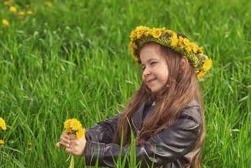 Portrait of a little girl in a dandelion wreath on a summer walk in the countryside