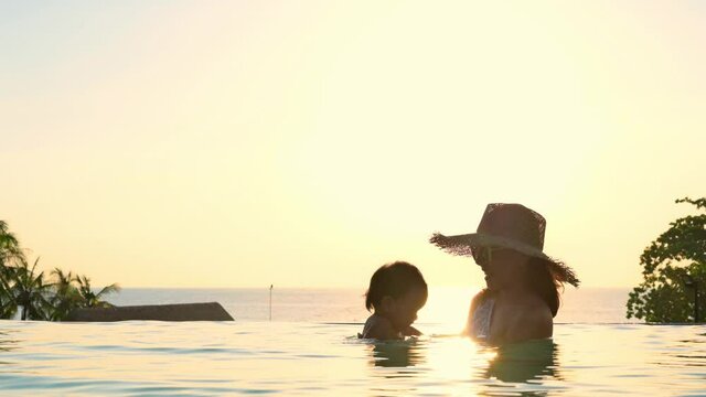 Asian mother and little son enjoying swimming in a swimming pool in summer vacation.