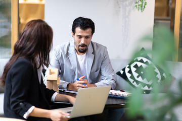 Beautiful woman real estate agent offering and showing online presentation on laptop in office to handsome man.