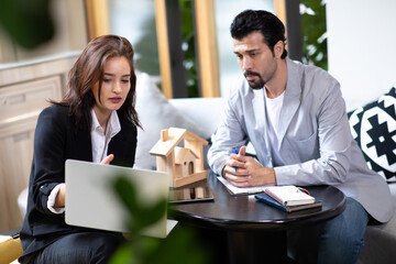 Beautiful woman real estate agent offering and showing online presentation on laptop in office to...