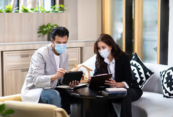 Beautiful woman real estate agent offering and showing online presentation on laptop in office to handsome man. People wearing face mask protective corona virus.