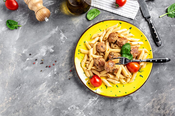 penne pasta with meatballs and tomato sauce, on a yellow plate and a gray background