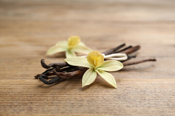 Fototapeta na wymiar Aromatic vanilla sticks and flowers on wooden table, closeup