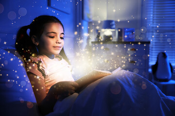 Little girl reading fairy tale in dark bedroom