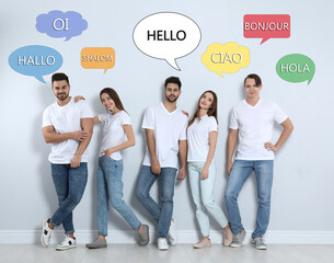 Happy people posing near light wall and illustration of speech bubbles with word Hello written in different languages © New Africa