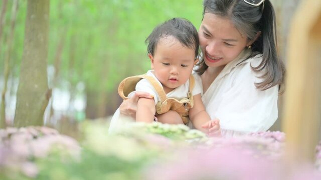 mother with little child in white blooming garden. woman with son in green leaves,happy family outdoors in spring