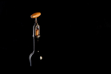 Red wine bottle with 2 glasses and bottle opener on black background.