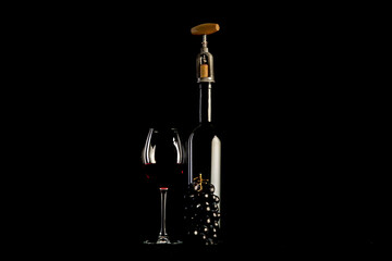 Red wine bottle with 2 glasses and bottle opener on black background.