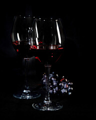 Red wine bottle with 2 glasses and bottle opener on black background.