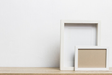 A white photo frames on table over the light wall.